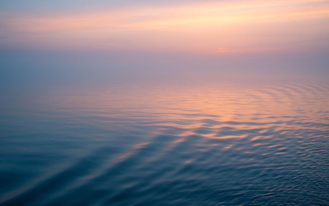 Peaceful ocean scene with calming ripples at sunset creating a gradient sky reflection.
